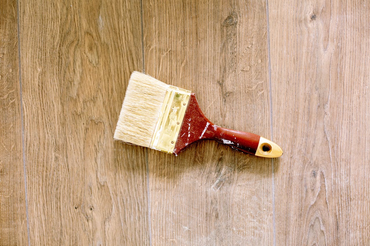 about-img-01 A used paintbrush lying on a wooden floor, ideal for renovation and DIY themes.